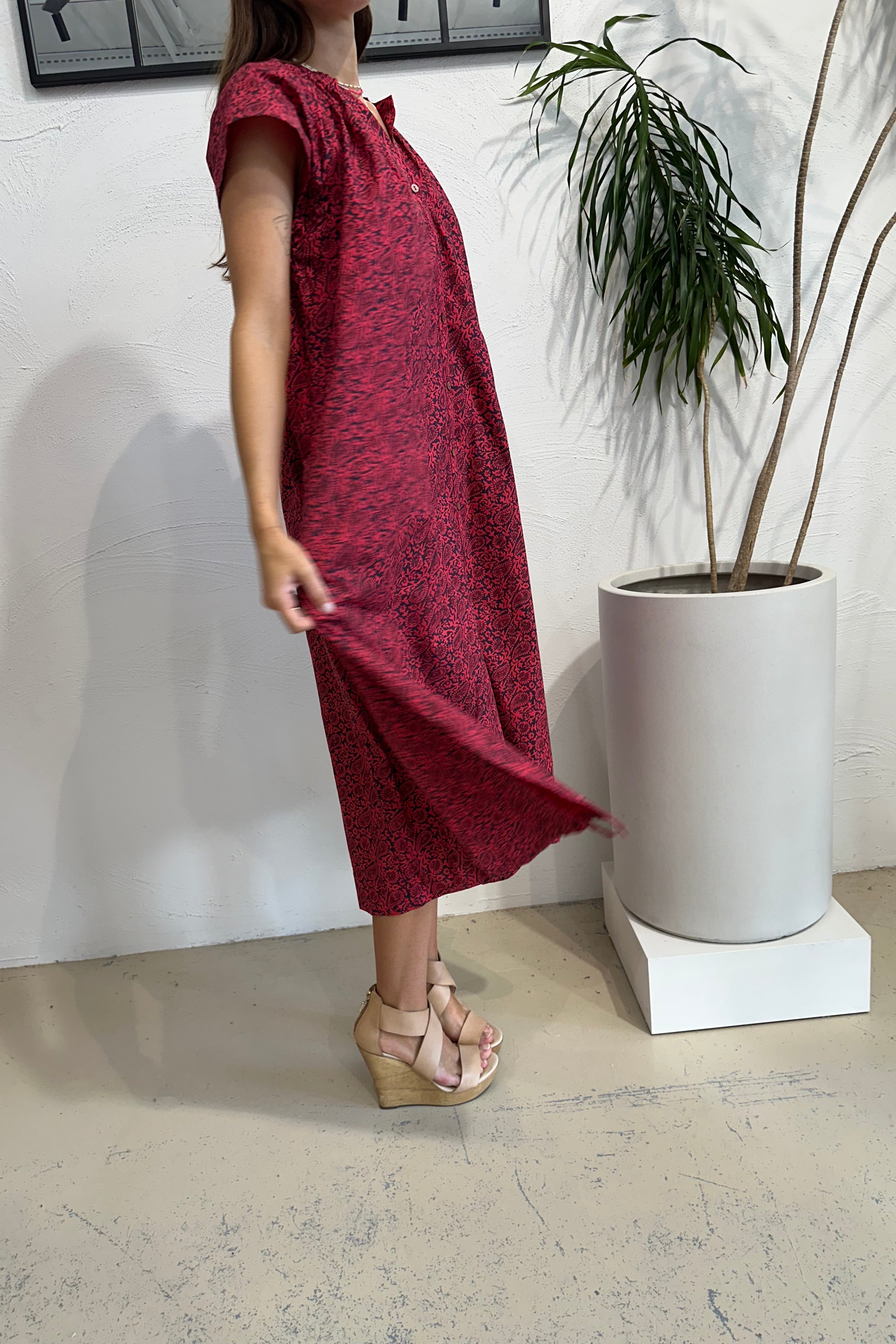 Person wearing a red dress and high heels on a light-colored floor with a plant in the background