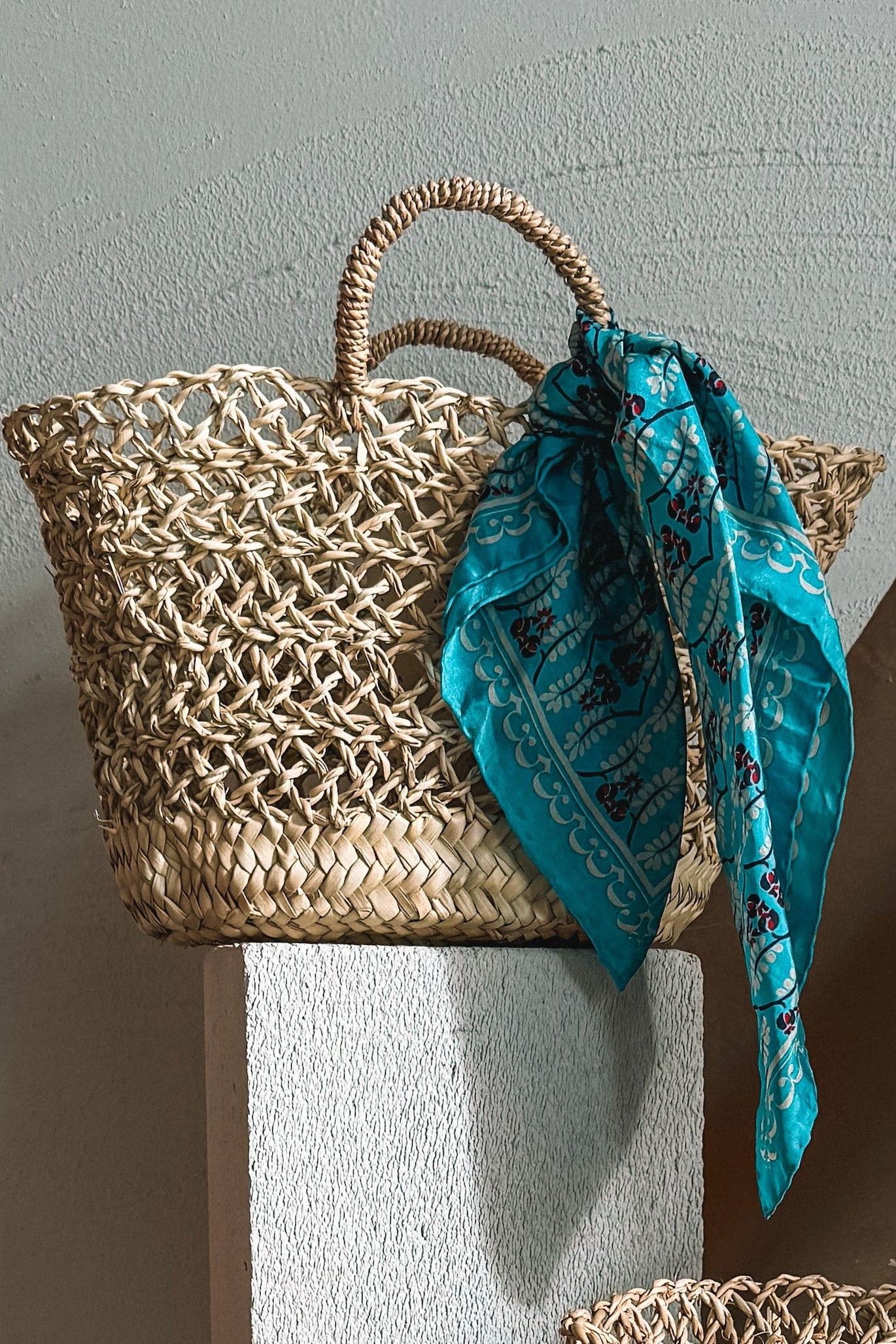 Three woven bags with scarves on a neutral background