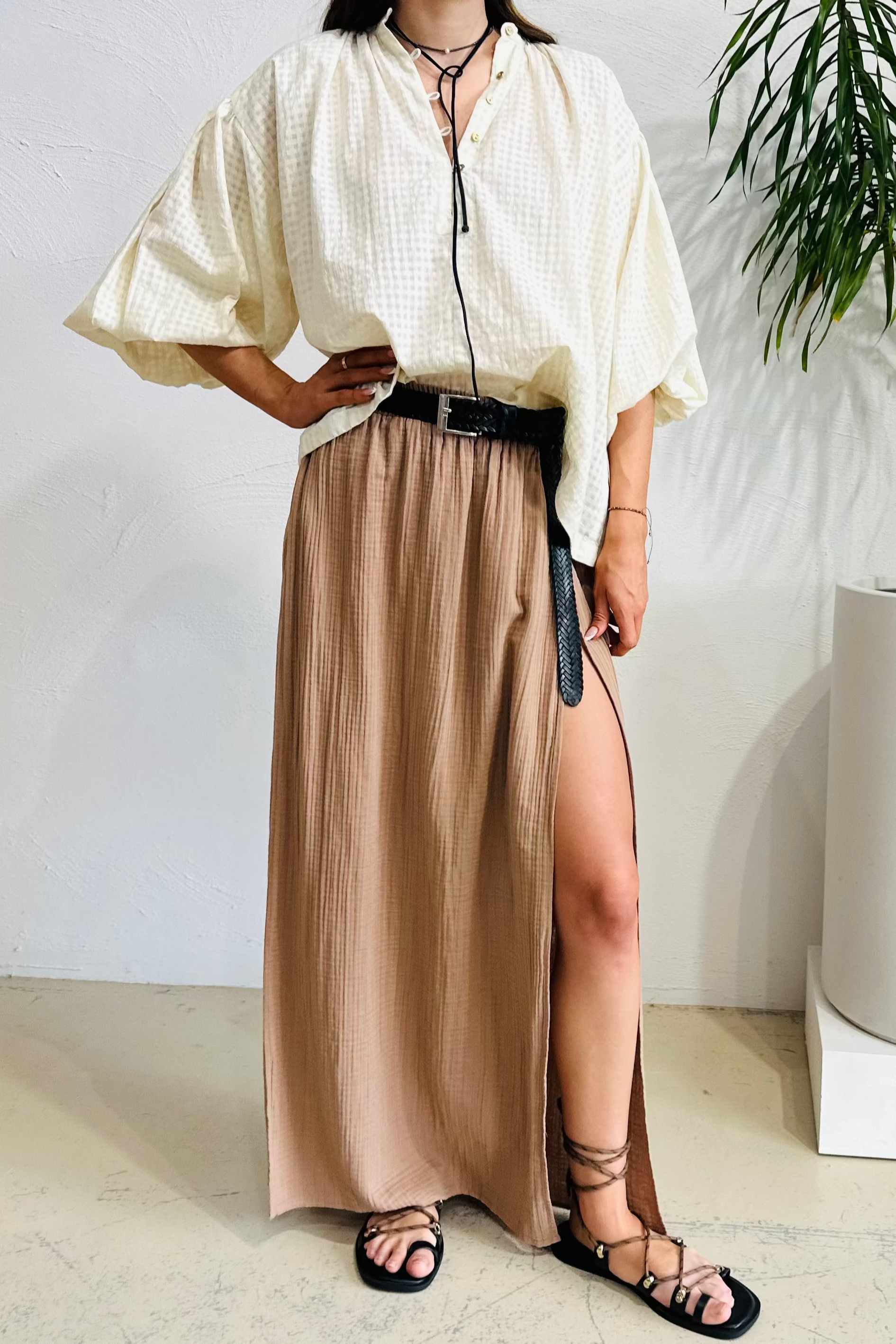 Woman in a white blouse and beige skirt standing indoors with a plant in the background