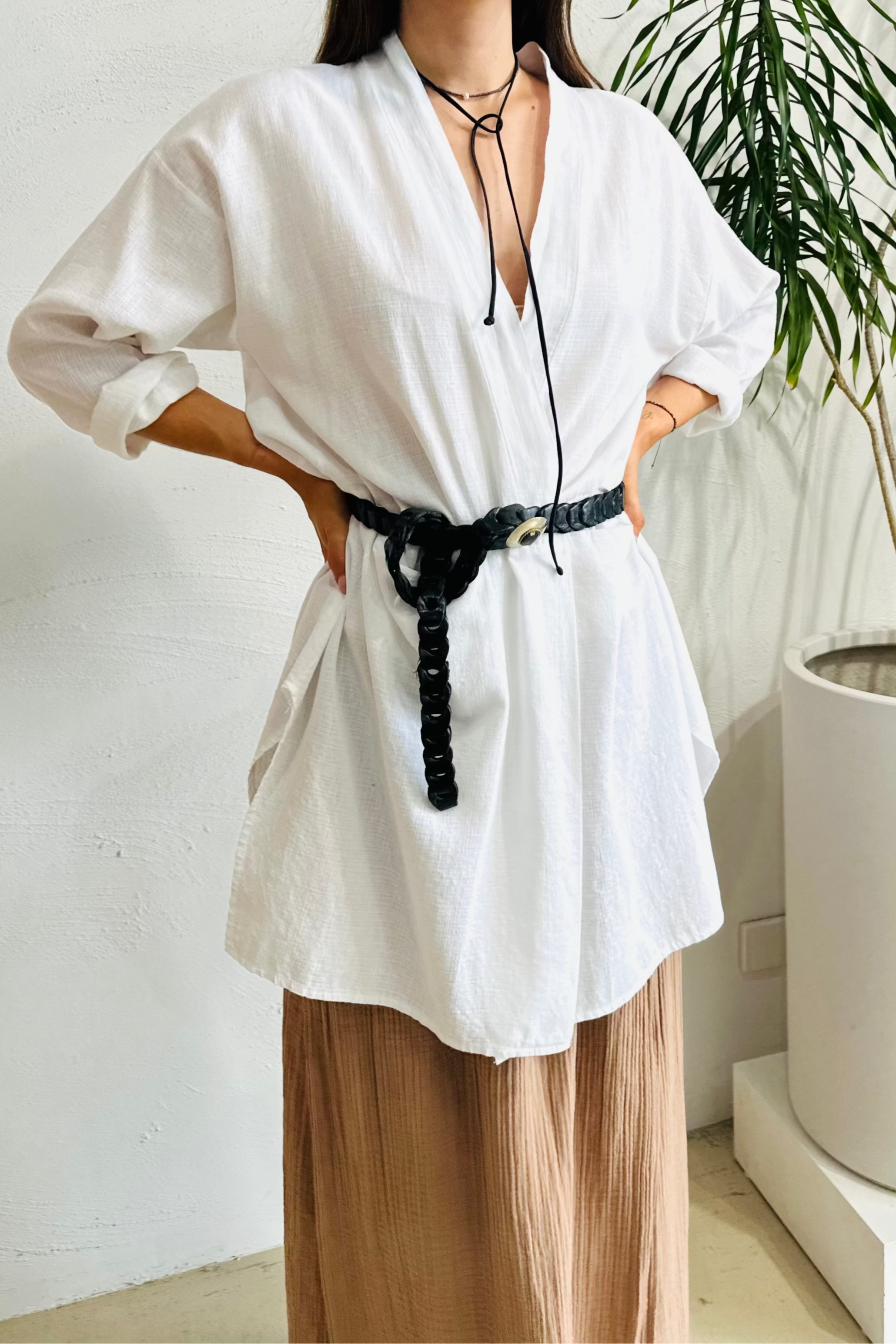 Person wearing a white blouse with a black belt and brown pants in an indoor setting.
